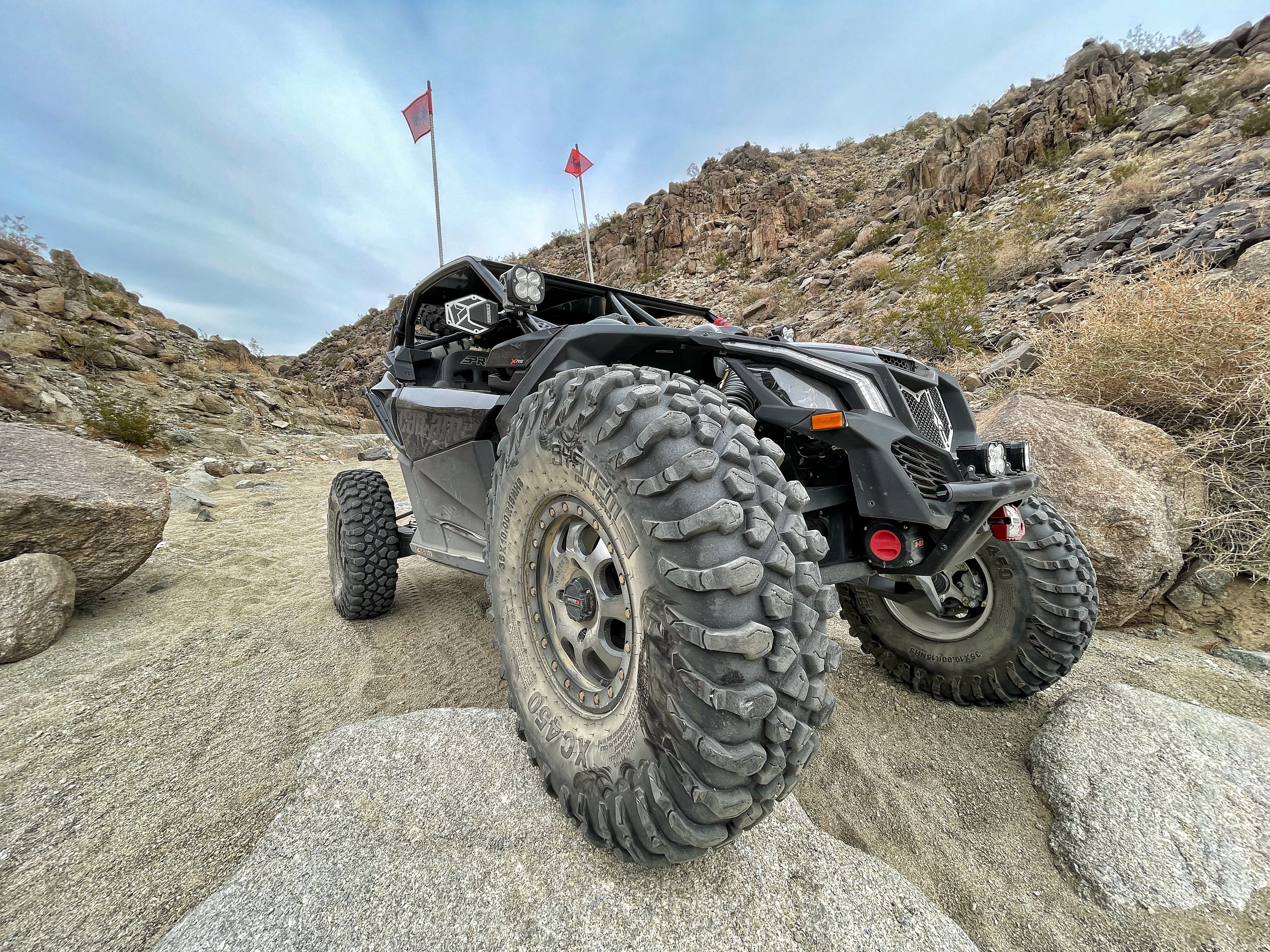 Custom-built black Can-Am side-by-side going downhill with its right front wheel on a rock.