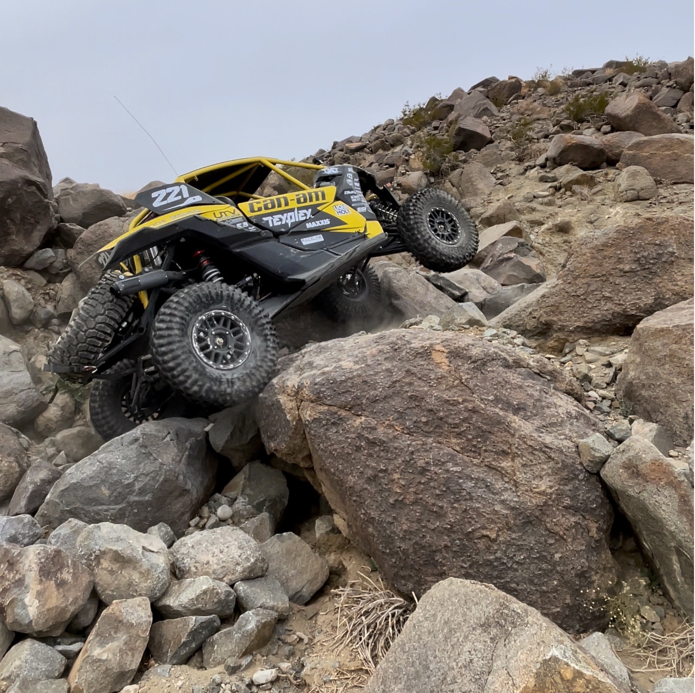 Custom-built black and yellow Can-Am side-by-side leaning to the left as it crawls up large rocks.
