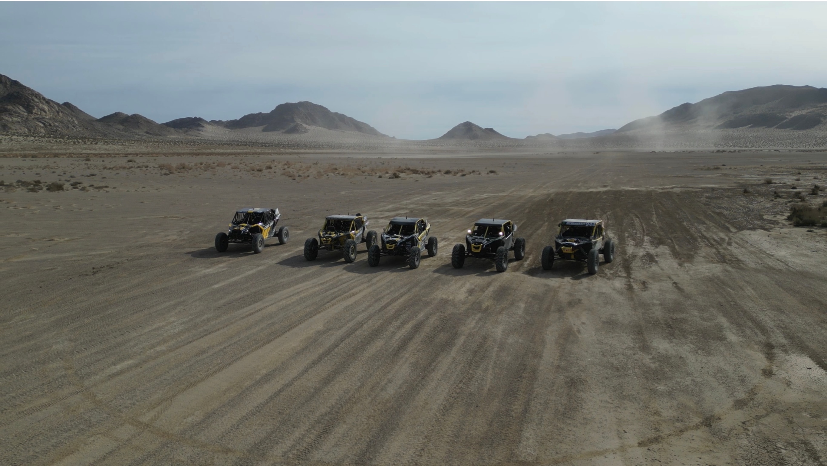 Une rangée de véhicules côte à côte Can-Am jaune et noir, personnalisés, stationnés à l’extérieur dans la boue
