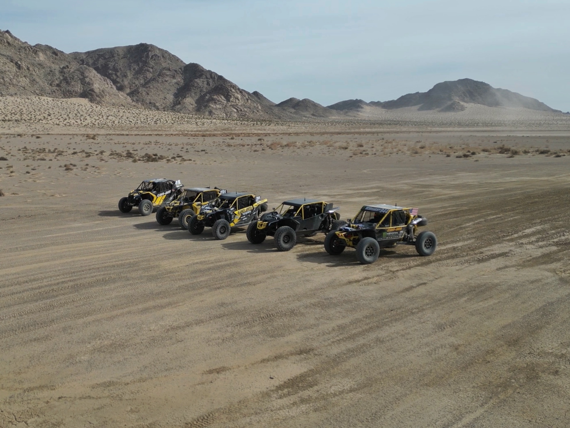 A row of custom-built Can-Am side-by-sides driving next to one another on a dirt trail.