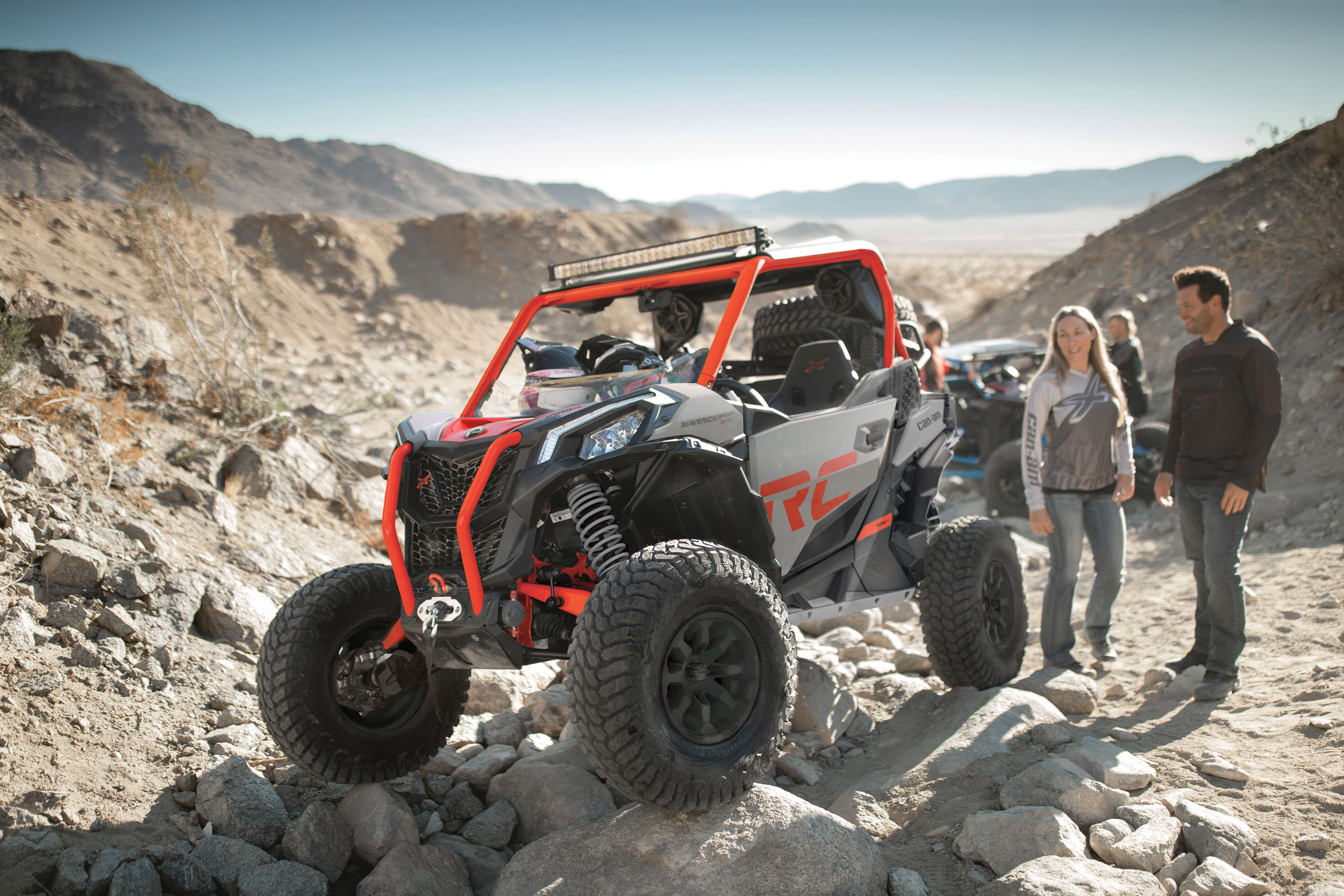 Two people looking at a parked Can-Am Maverick Sport X rc side-by-side on rocks