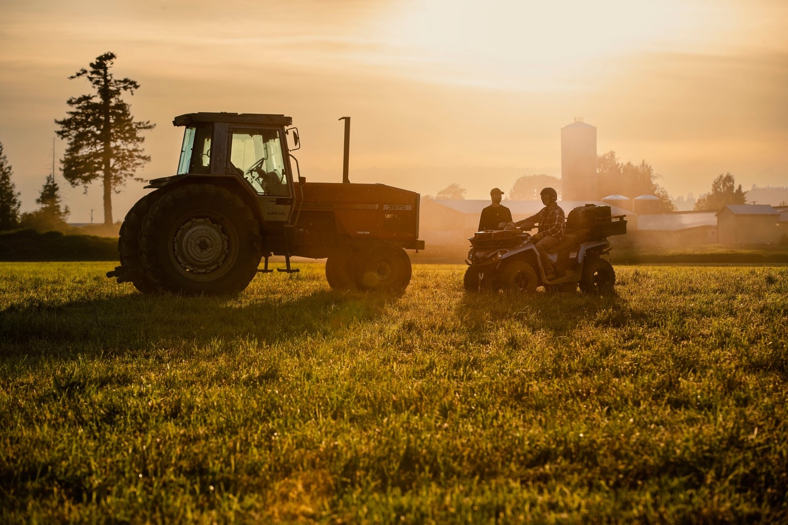 Two men with an ATV and a tractor in field