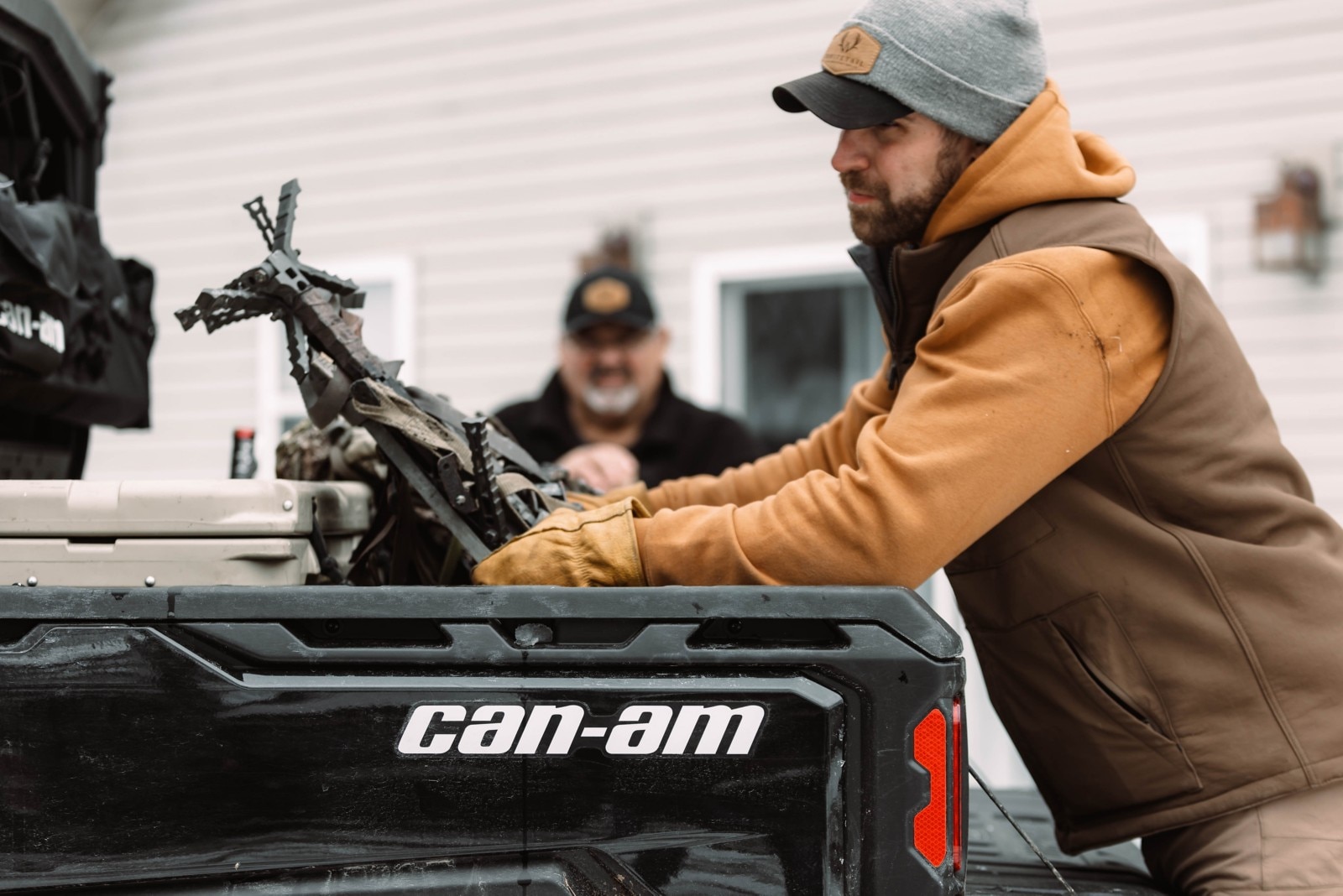 Brett Smith loading hunting gear into the box of his Can-Am Defender with his dad watching in the background. 