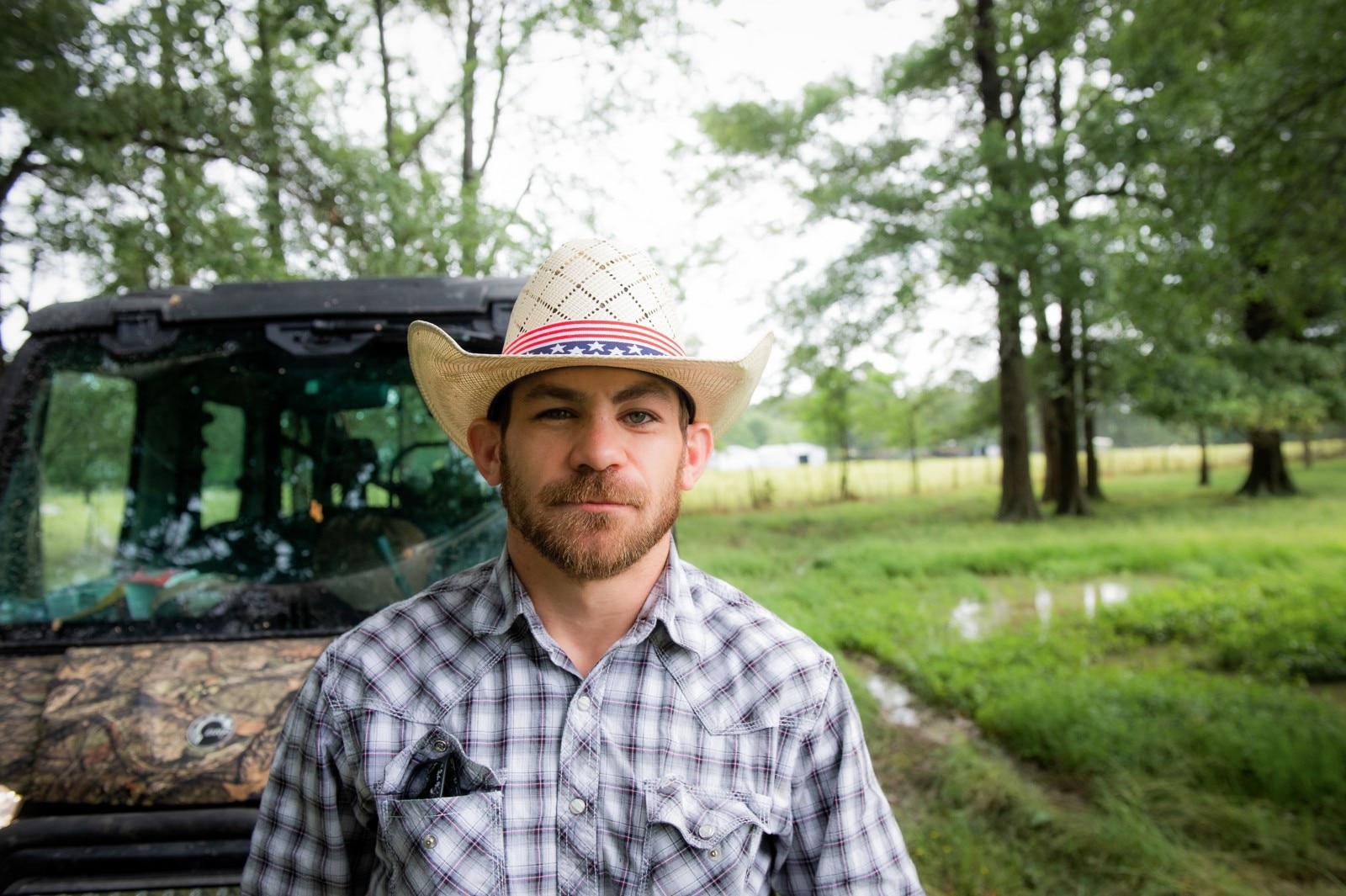 Chase Outlaw posing in front of his Mossy Oak Defender on his land, wearing a cowboy hat