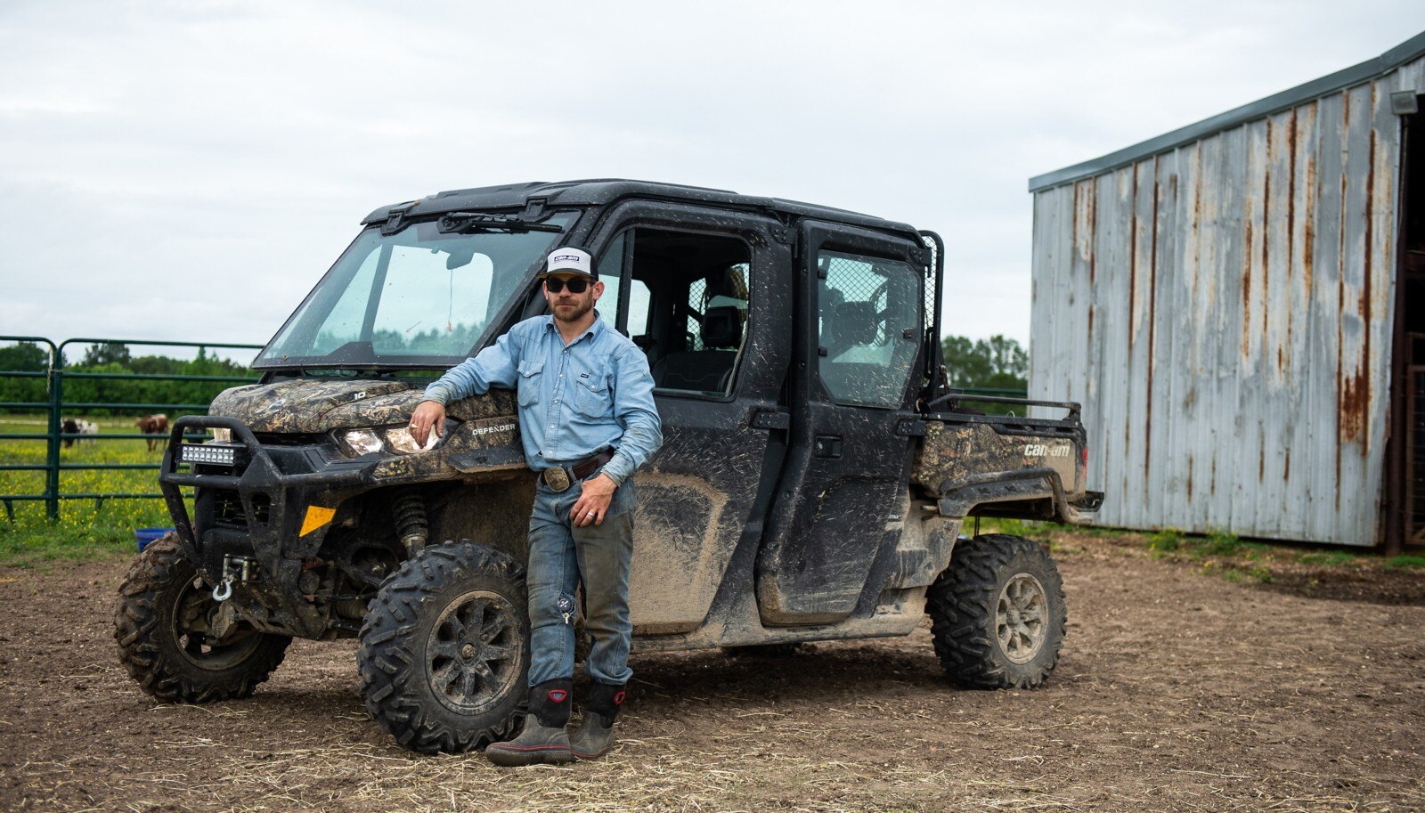 Chase Outlaw leaning against his Defender parked in front of a pasture and farm building.
