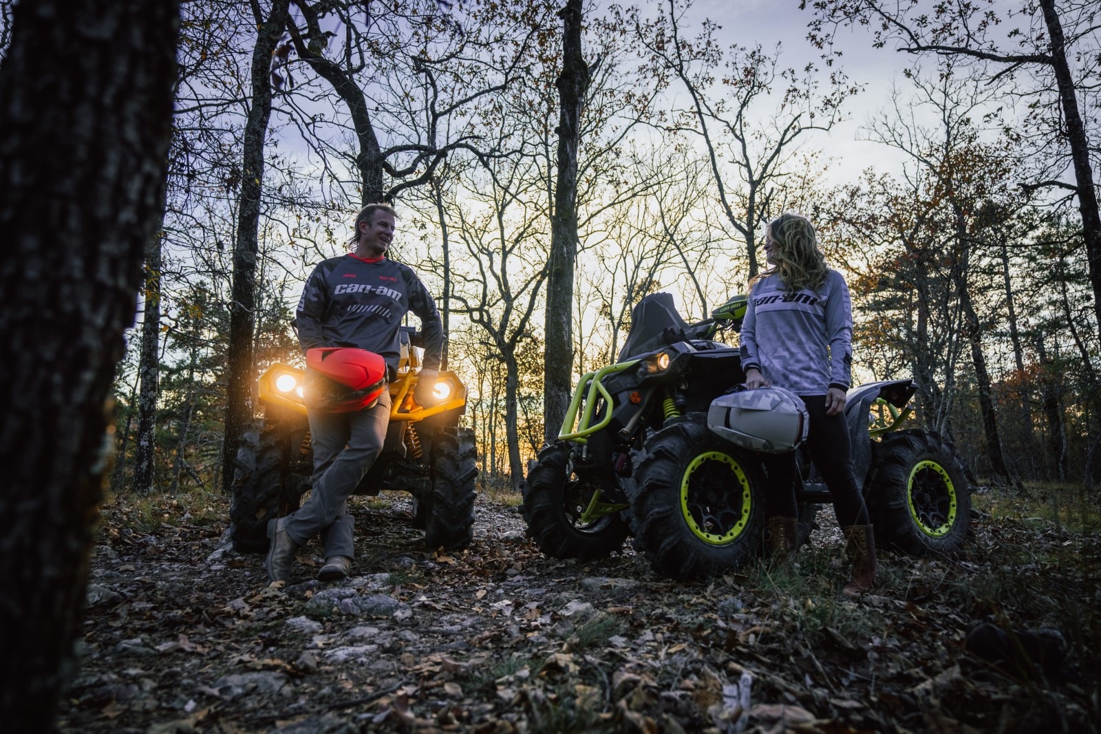 Two ATV riders dressed in Can-Am apparel with the sun setting behind.