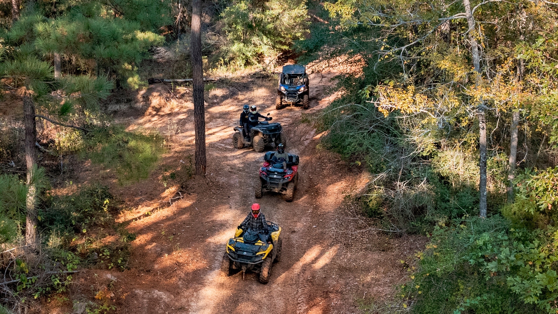 Riders driving Can-Am side-by-side and all-terrain vehicles on a trail in the forest