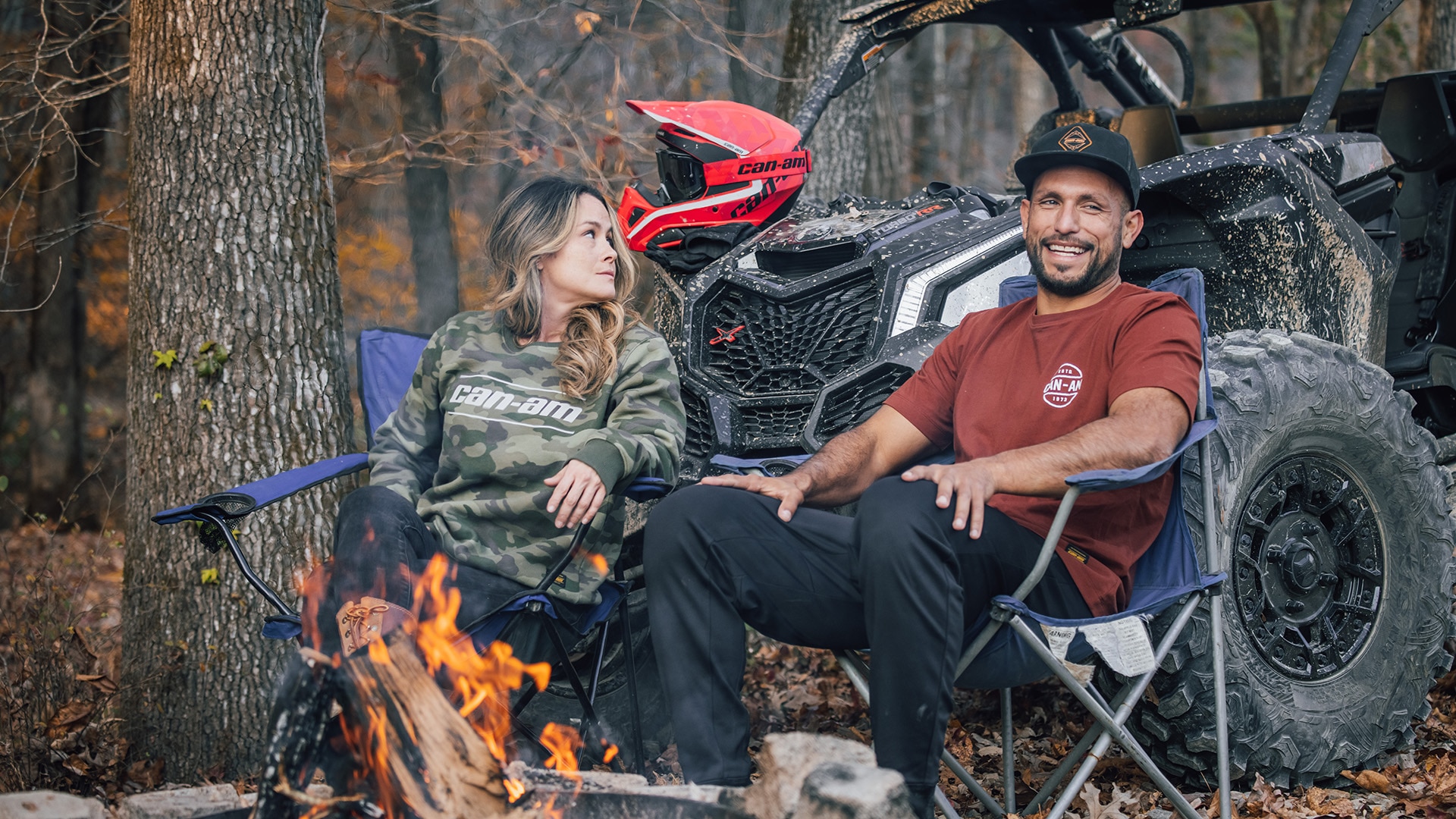 Two riders sitting around a fire in their Can-Am apparel