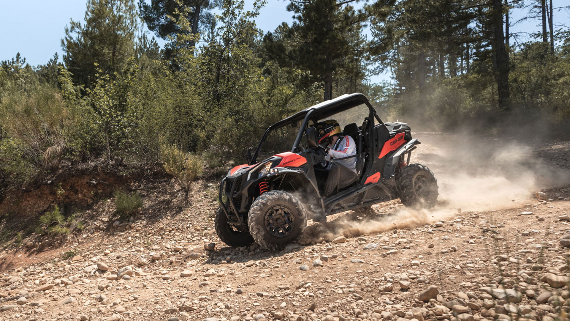 A Can-Am Maverick Trail with two passengers wearing Pyra helmets in an adventure setting