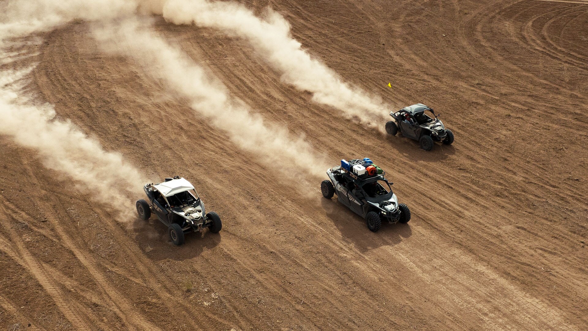Can-Am Maverick side-by-sides kicking up clouds of dust and driving together on a trail.