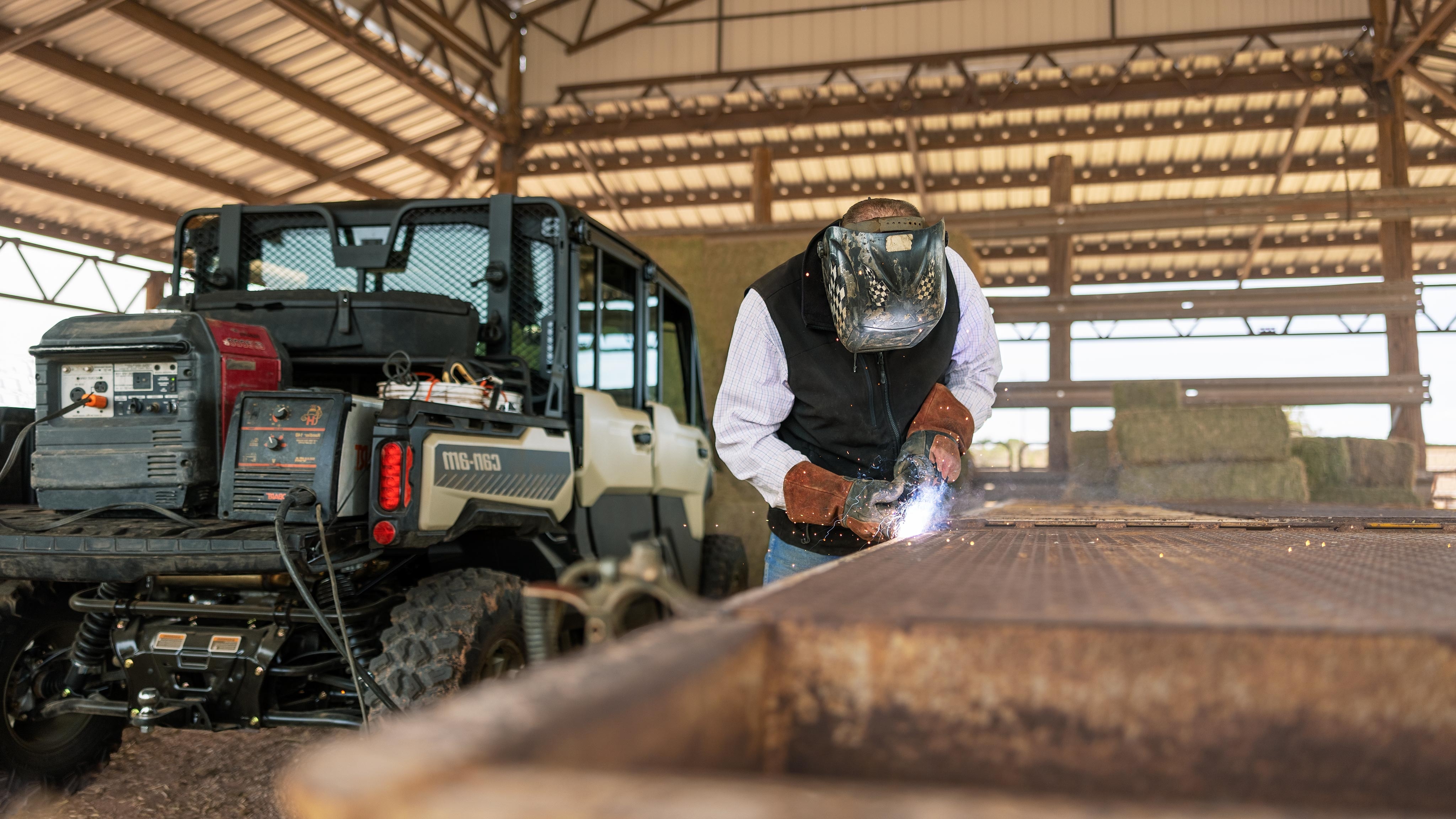 A welder working in front of their Desert Tan and Timeless Black Can-Am Defender Limited