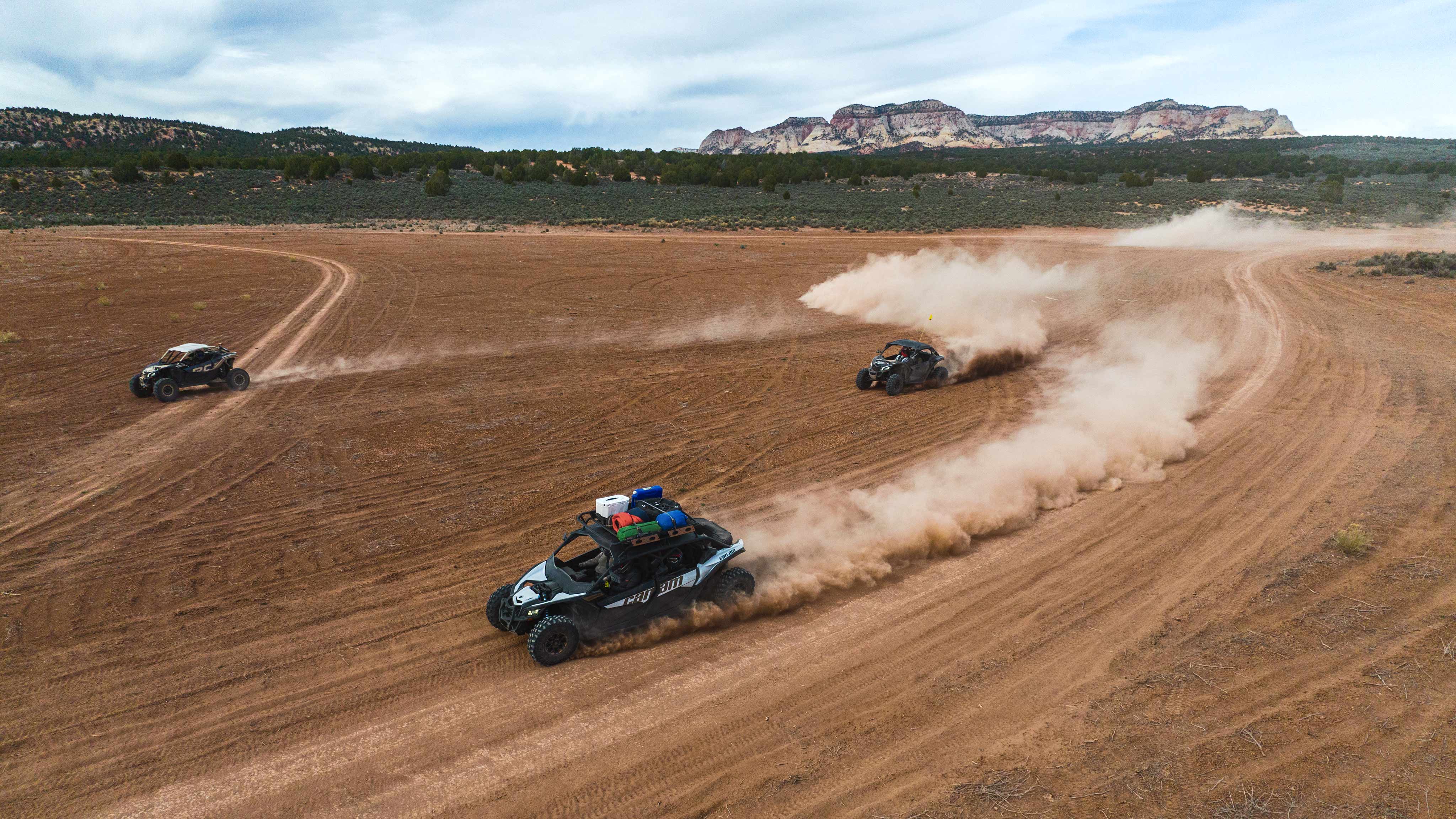 Can-Am Maverick side-by-sides kicking up clouds of dust and driving together in a desert setting