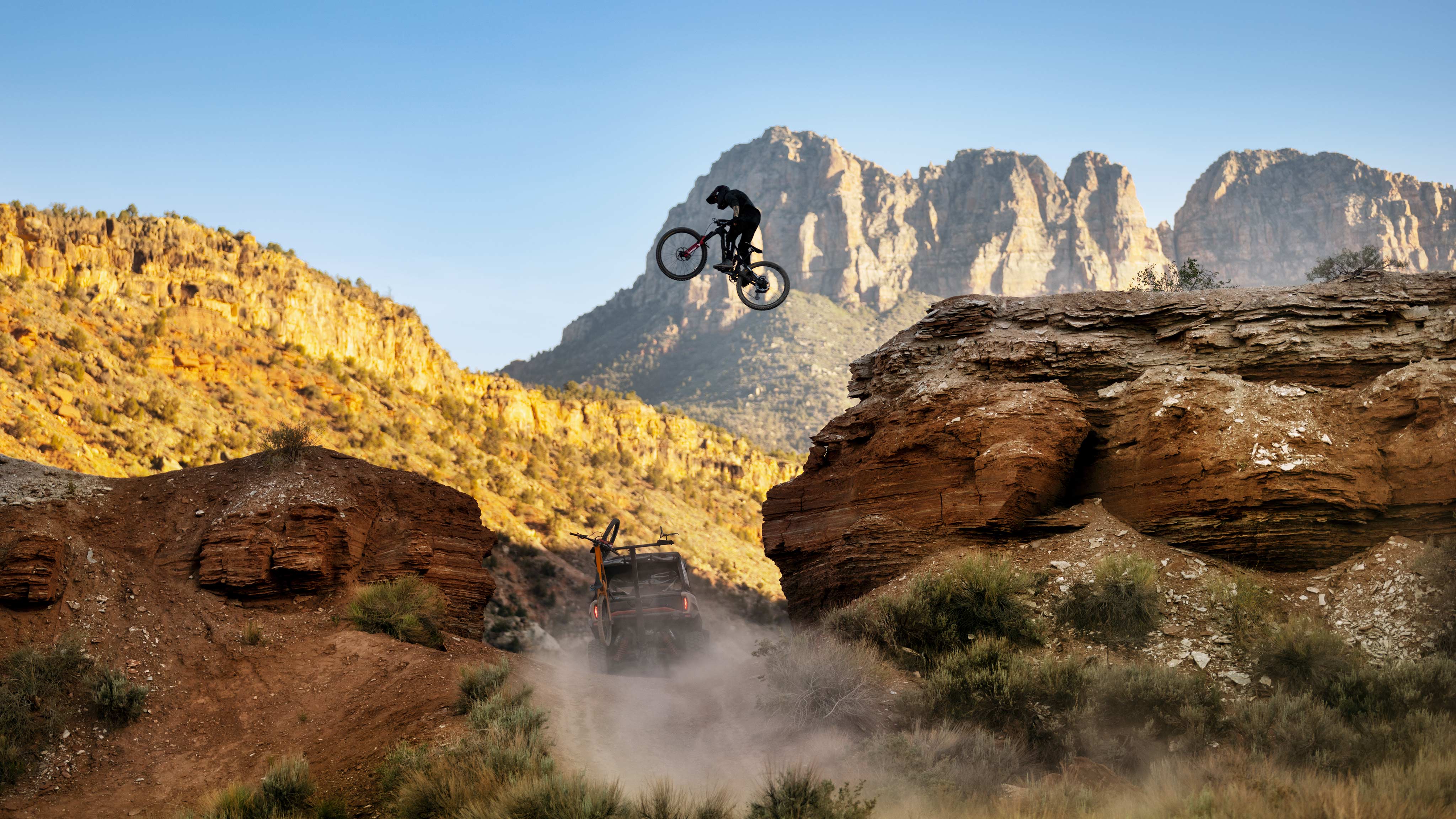 Un ciclista de montaña saltando sobre un Can-Am Commander XT-P desert tan & carbon black 