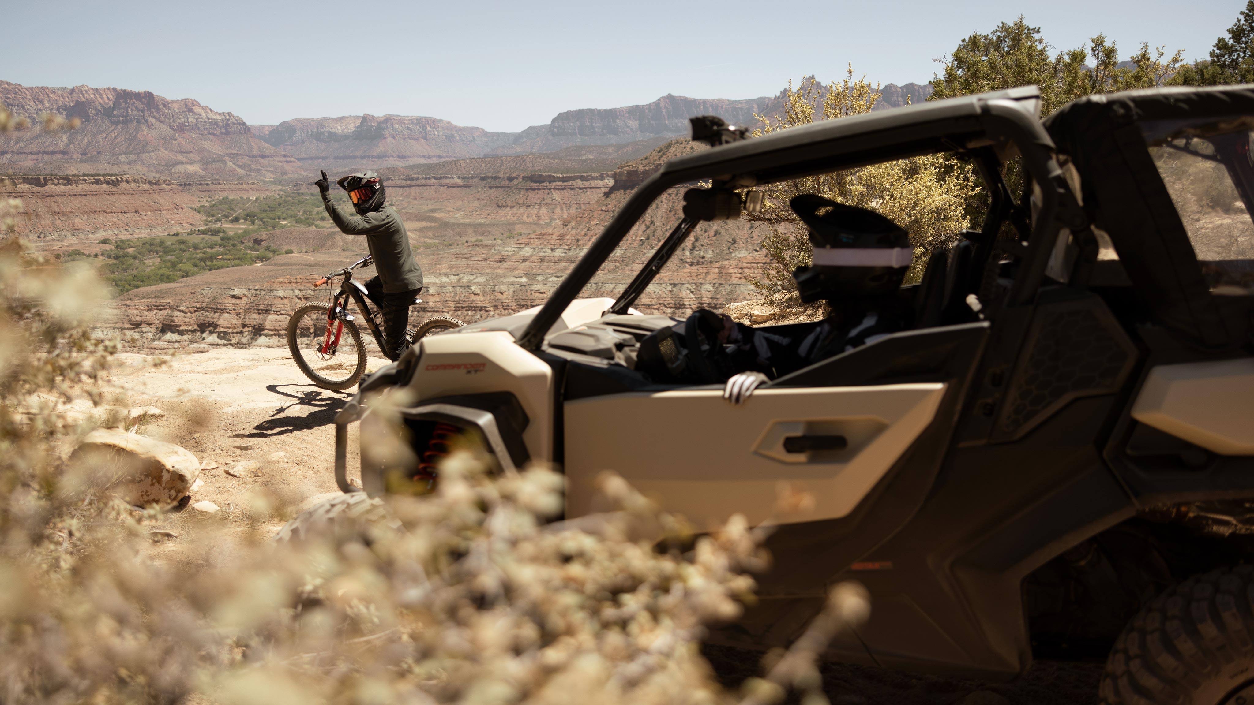 A mountain biker waving to the driver of a Desert Tan & Carbon Black Can-Am Commander XT-P