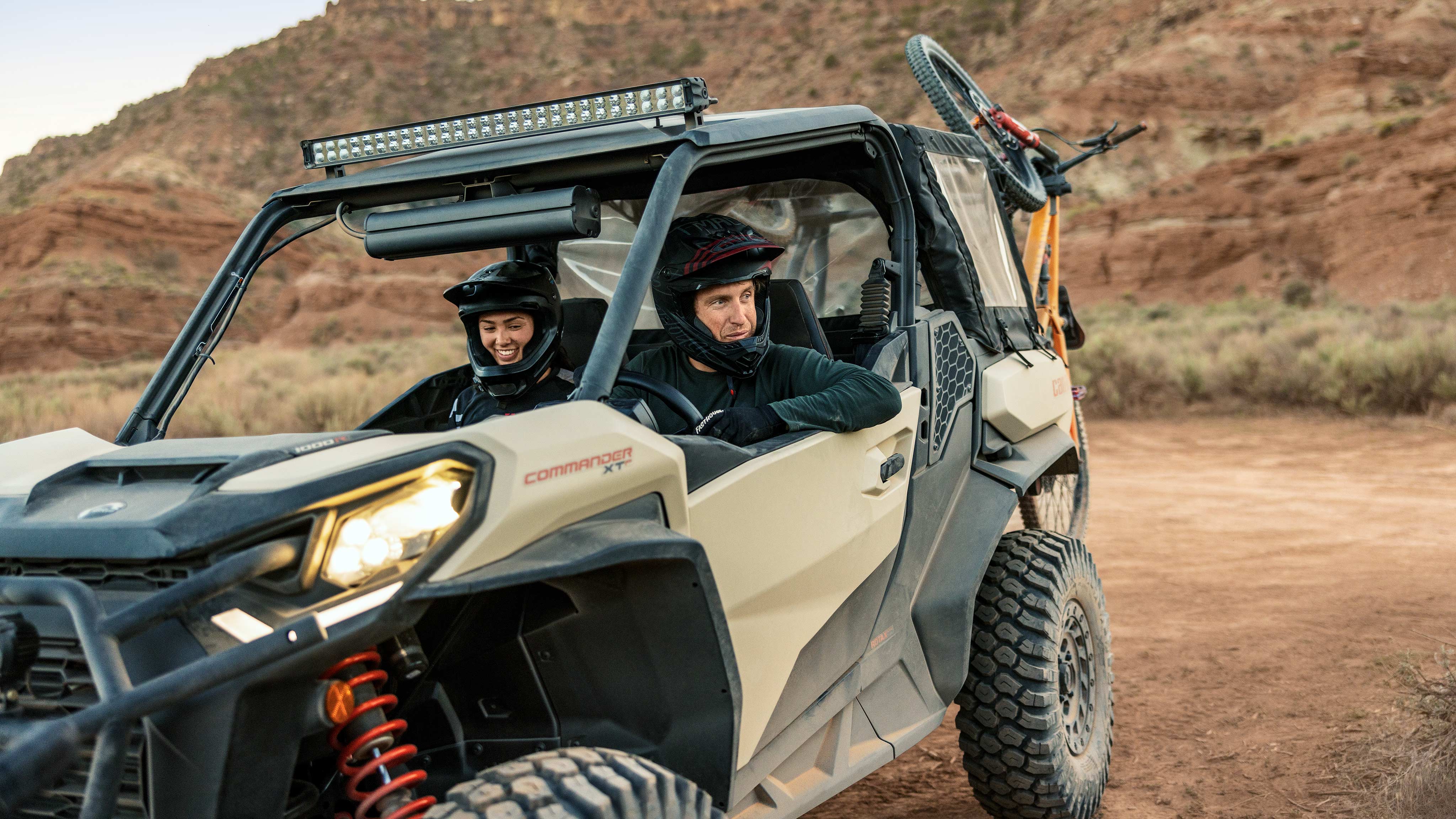 A couple sitting in their Desert Tan and Carbon Black Can-Am Commander XT-P, wearing Pyra Helmets on an adventure.