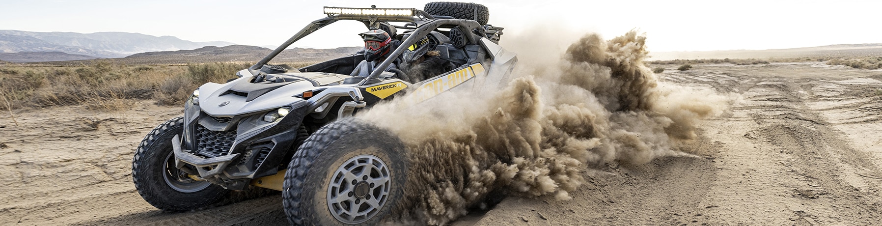 Two riders in a Can-Am Maverick R SxS vehicle speeding through the desert