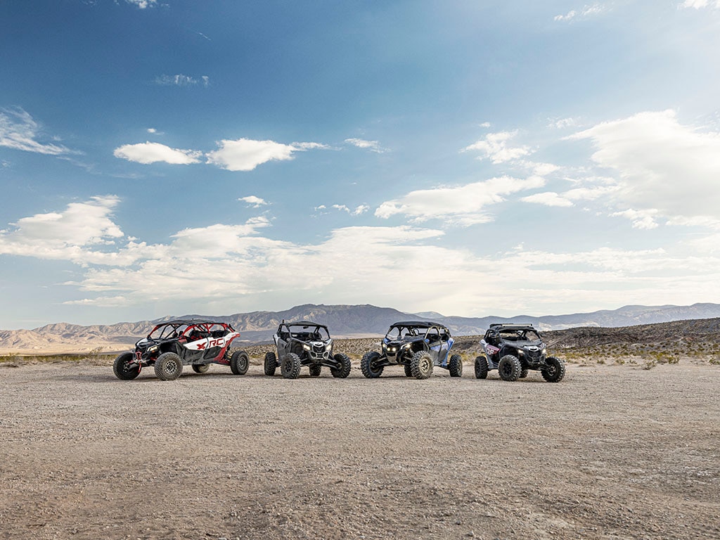 Quatre véhicules côte à côte Maverick X3 stationnés dans le désert devant des montagnes