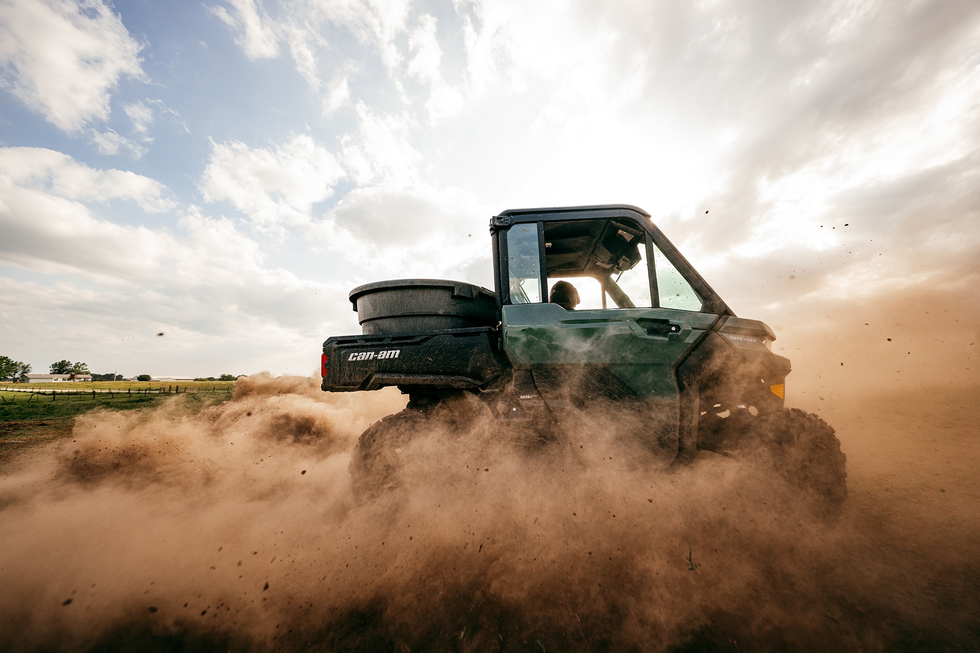 Can-Am Defender DPS 2027 compass green side-by-side, en medio del polvo de un campo