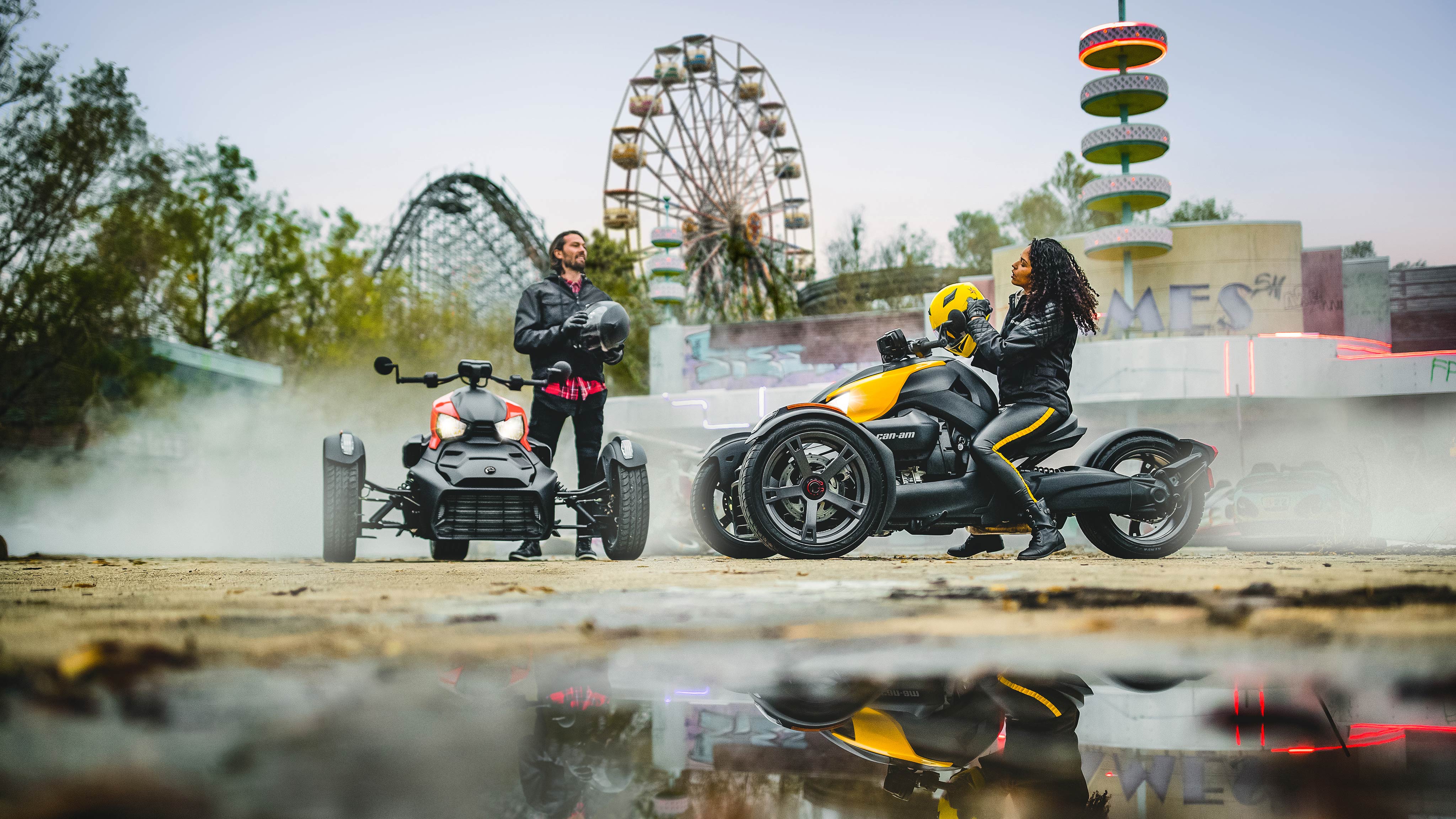 Deux amis garés devant un parc d’attractions avec leurs motos Can-Am Ryker, un avec panneaux Rouge adrénaline et l’autre avec panneaux Jaune vif