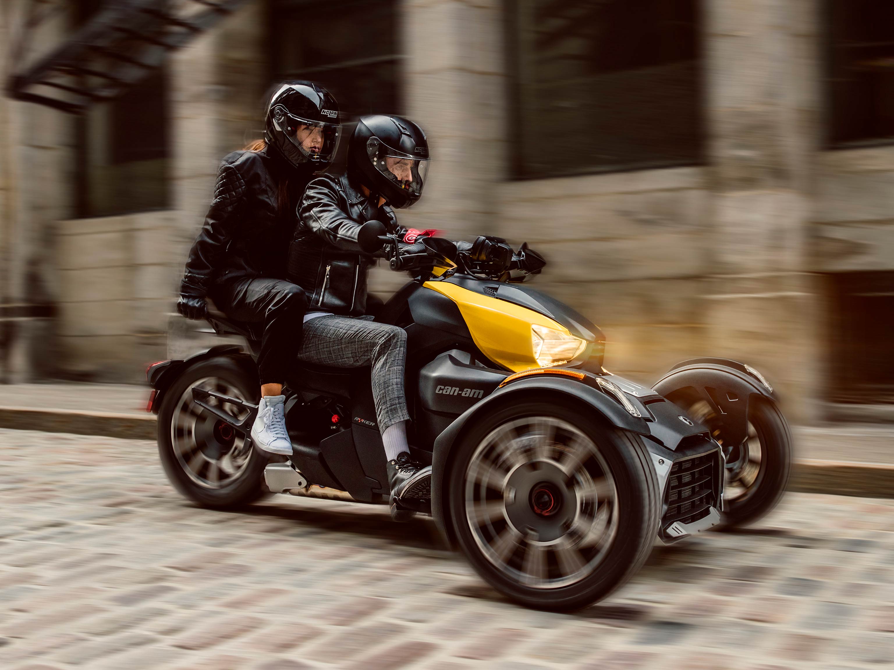 A couple riding a Can-Am Ryker with yellow shock panels along a cobblestone street