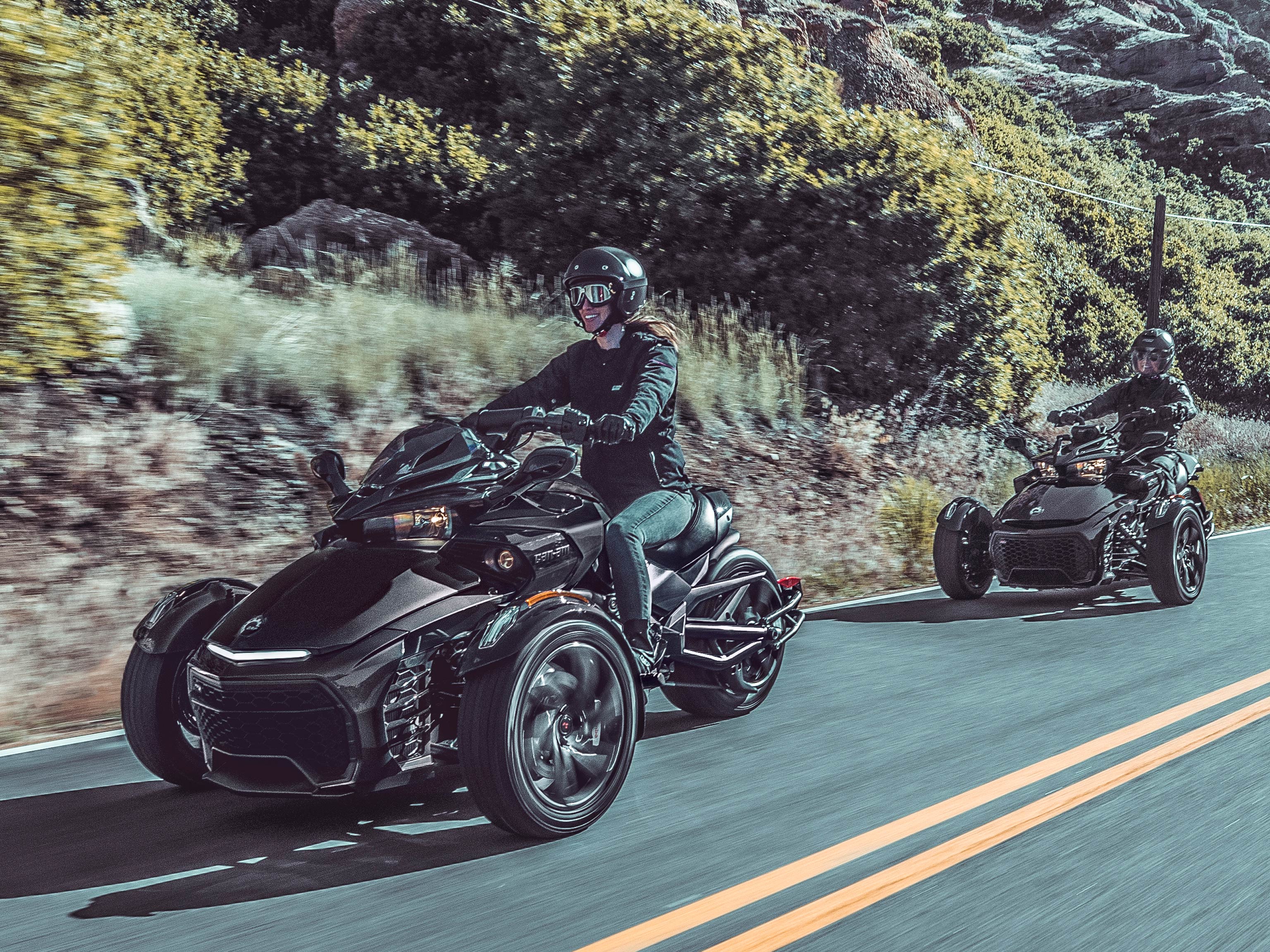 Dos personas conduciendo sus vehículos Can-Am Spyder por carretera abierta en un entorno desértico