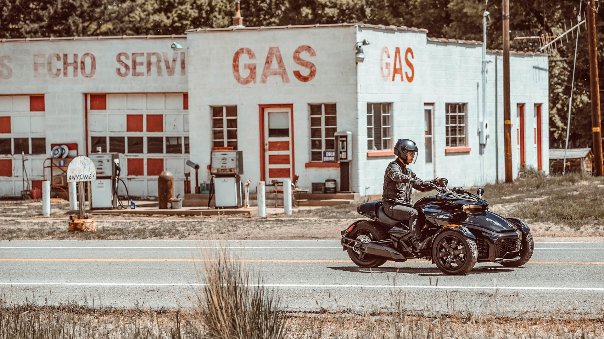 Man riding a Can-Am Spyder F3 in front of an old gas station