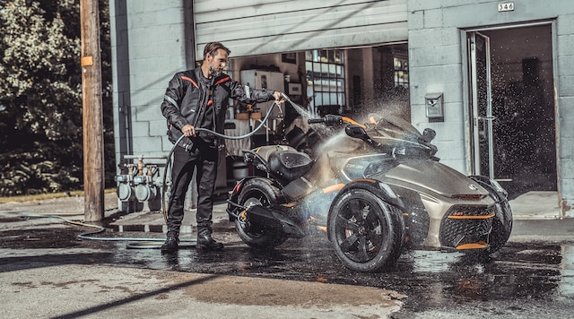 A male rider cleaning his Can-Am three-wheeler in front of his garage