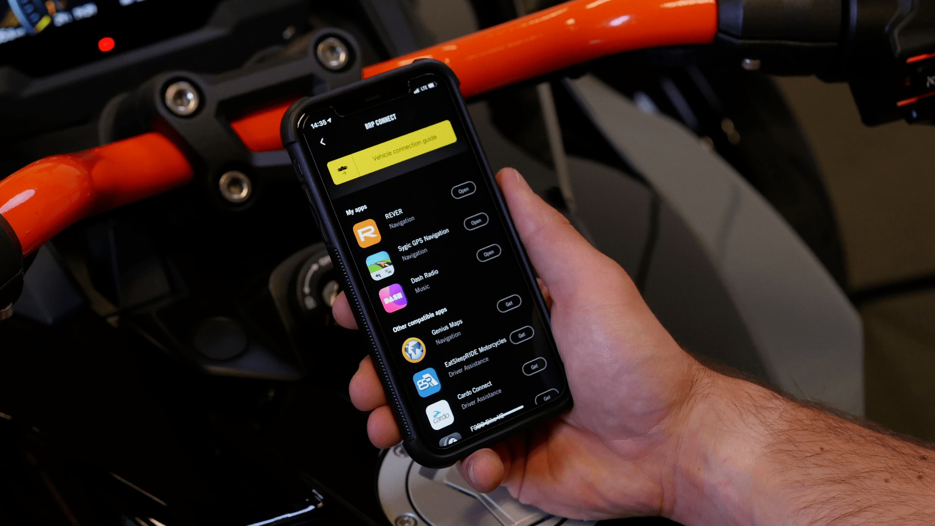 Someone holding a smartphone with the BRP GO! app next to a Can-Am Spyder vehicle