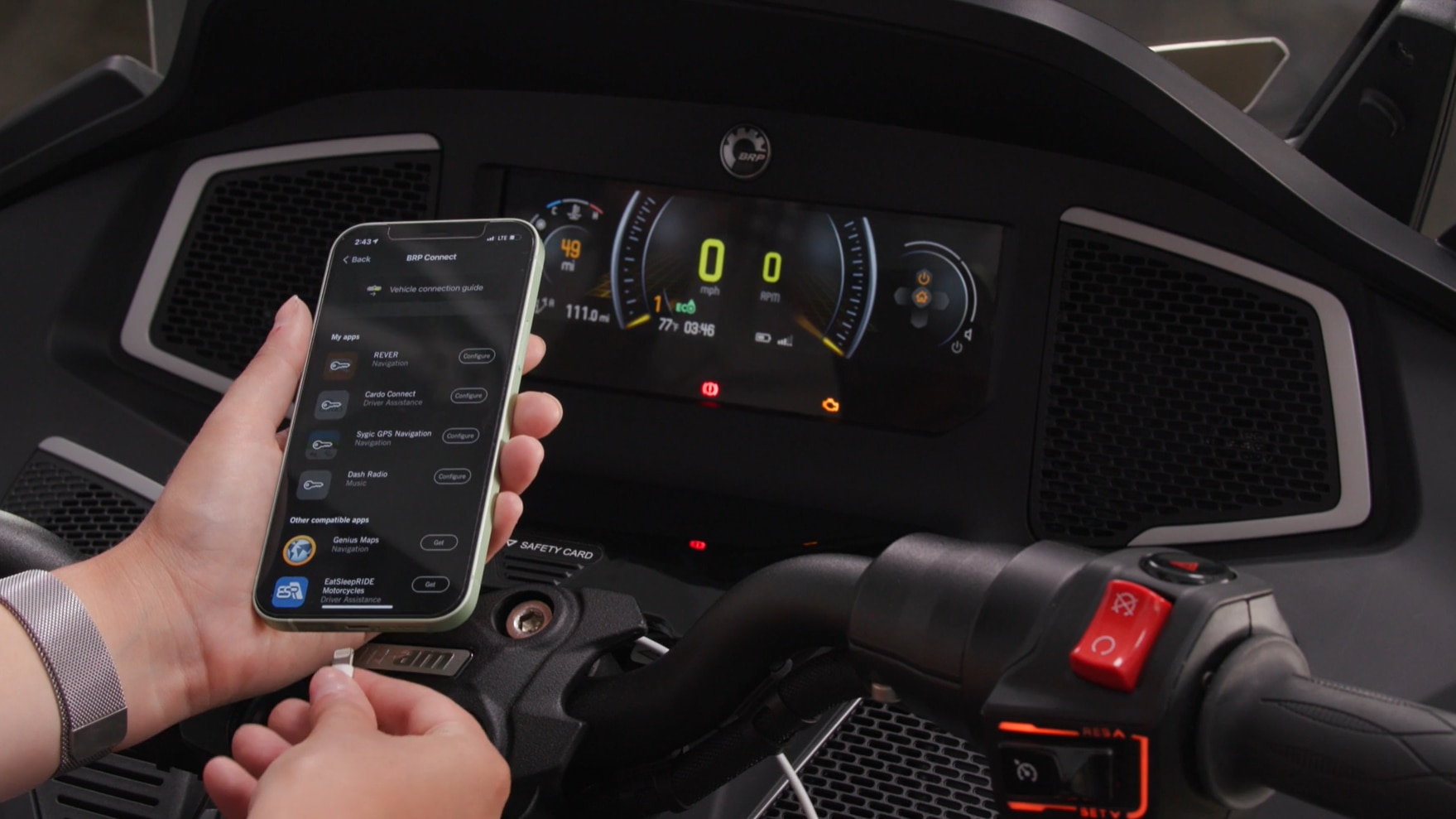 Fahrer mit einem Smartphone mit BRP GO! App neben einem Can-Am Spyder