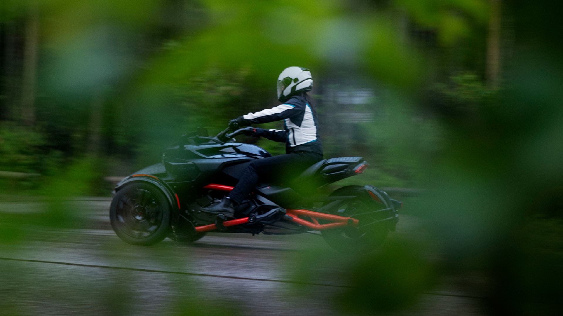 Woman riding a Can-Am 3-wheel motorcycle near a forest