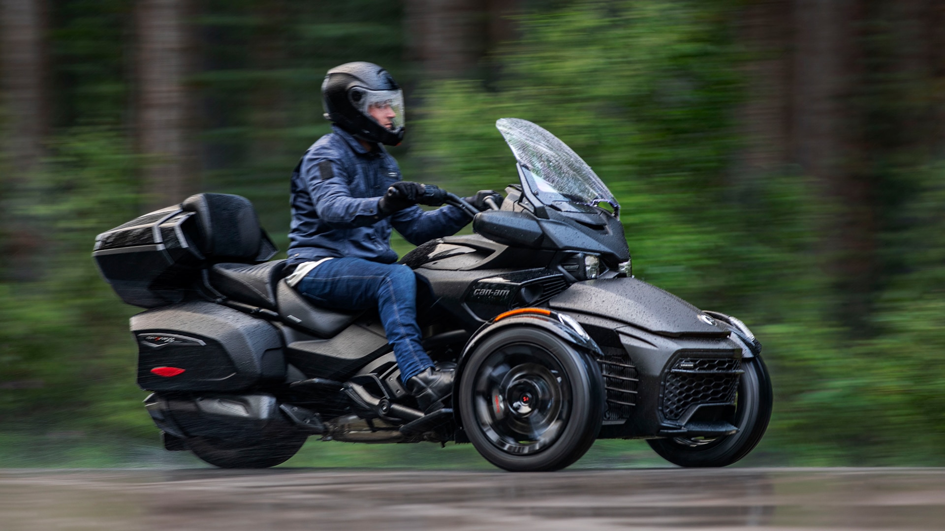 Man riding on his 2024 Can-Am Spyder F3 in the rain next to a forest