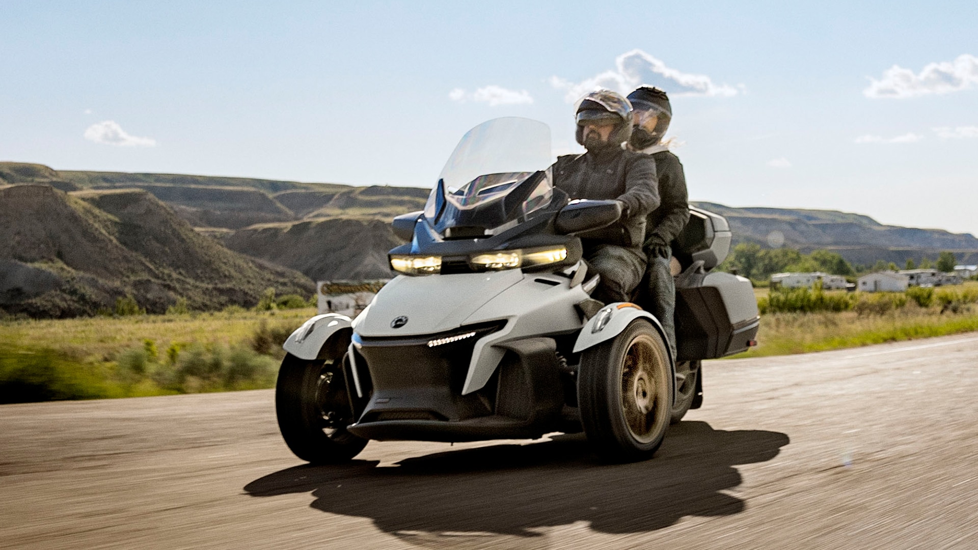 Two riders driving on their Can-Am Spyder RT next to a farm