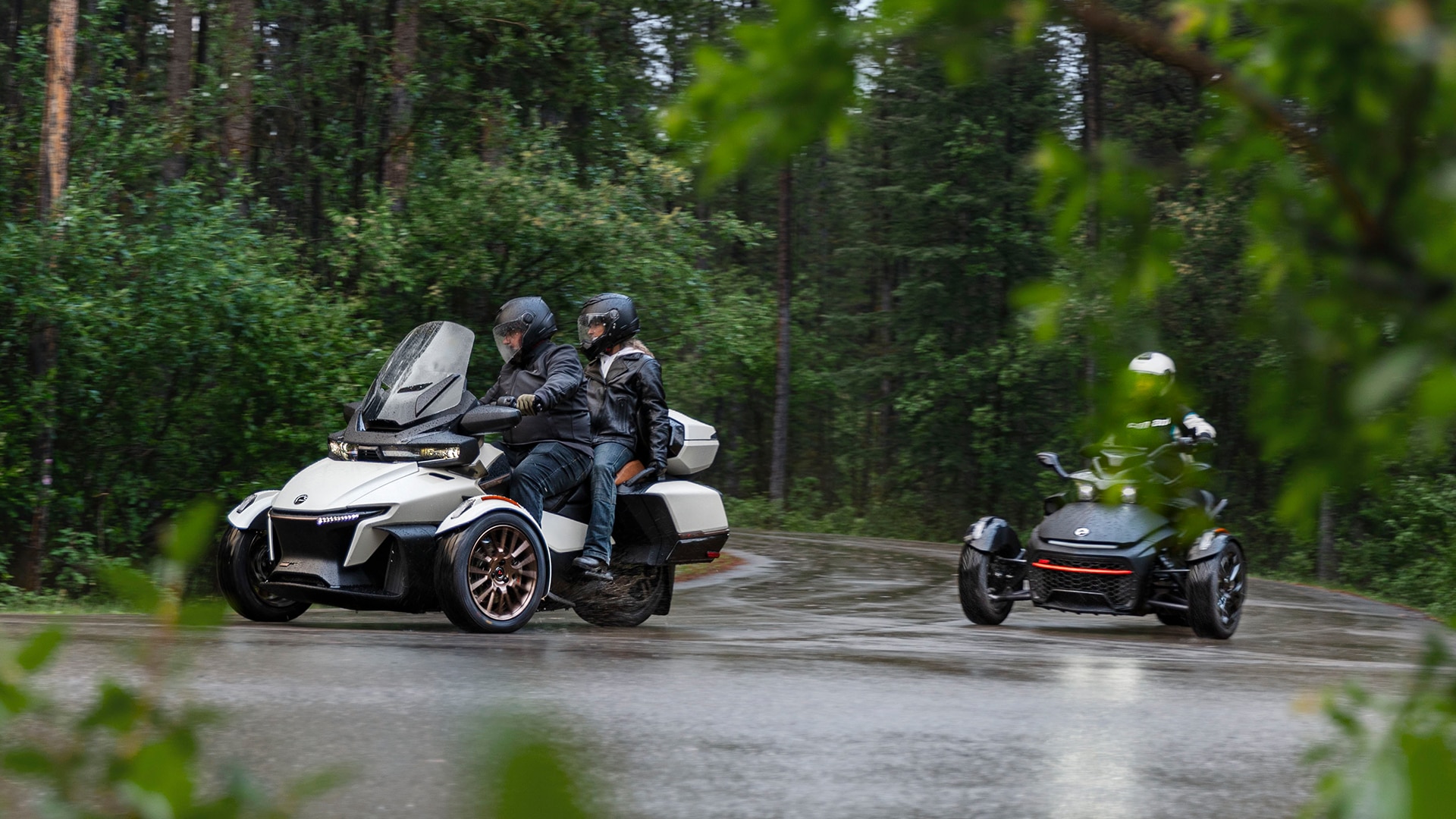 Two Can-Am Spyder RT 2024 turning in a tight corner on a rainy road in the forest