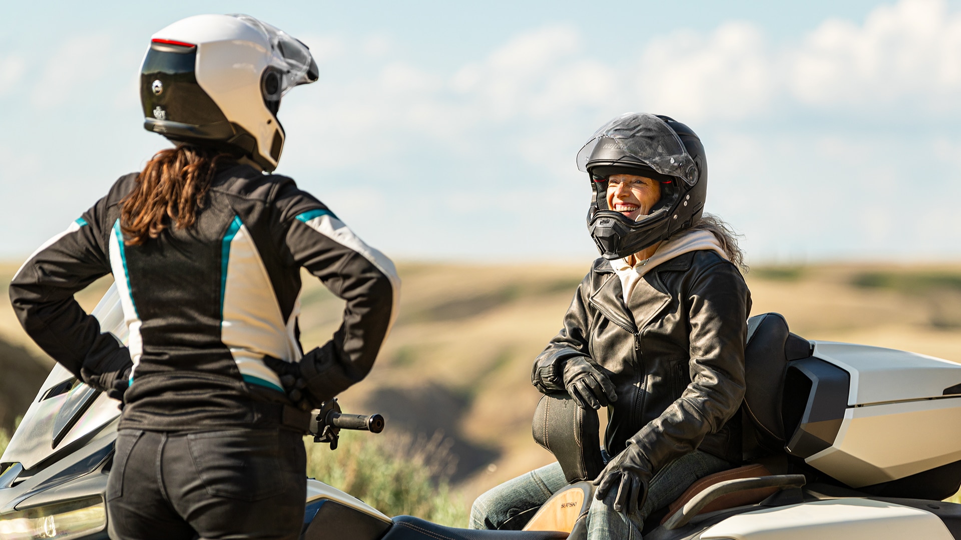 Two women talking and laughing on their 3-Wheel vehicle dressed in Can-Am apparel