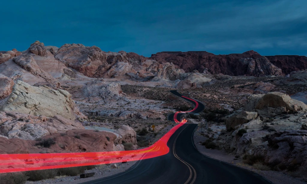 A winding valley road at the foot of a towering cliff face